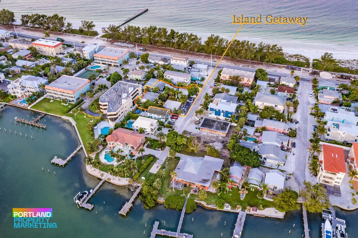 Aerial photo at dusk of a waterfront island neighborhood between a beach and a bay with private docks, with the featured property outlined and labeled Island Getaway.